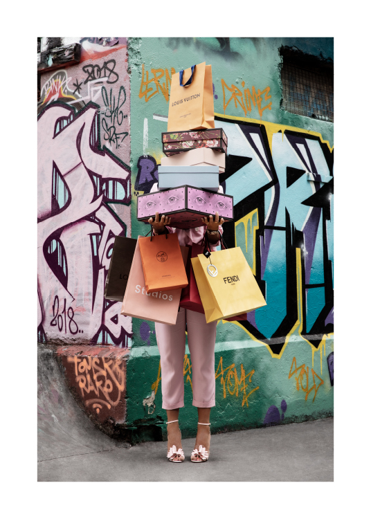  – Fotografia di una donna che tiene in mano una pila di shopping bag e scatole di scarpe, davanti a una parete con murales