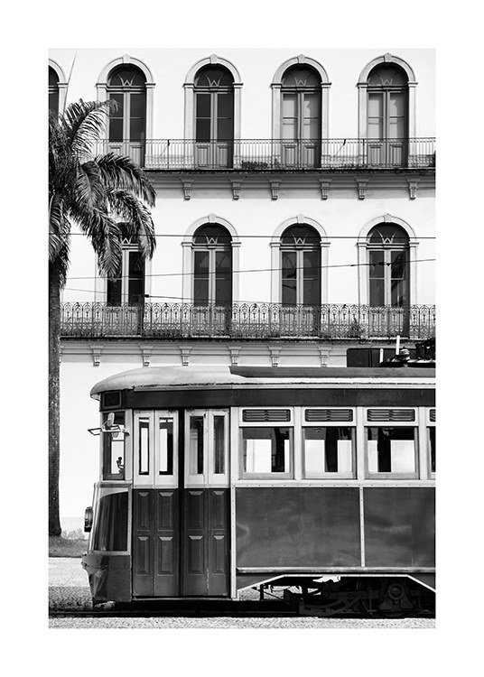  - Fotografia in bianco e nero di un edificio con balconi dietro un tram vintage, con una palma sul lato