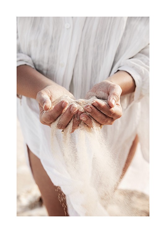  – Fotografia delle mani di una donna con sabbia tra le dita e la sua camicia di lino bianca in secondo piano