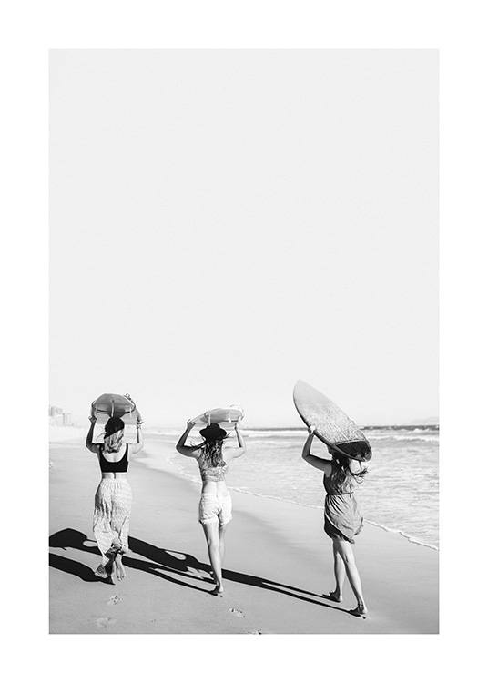  – Fotografia in bianco e nero di tre ragazze sulla spiaggia che trasportando le tavole da surf sopra la testa