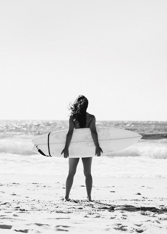 – Fotografia in bianco e nero di una ragazza che tiene una tavola da surf dietro di sé con l'oceano sullo sfondo