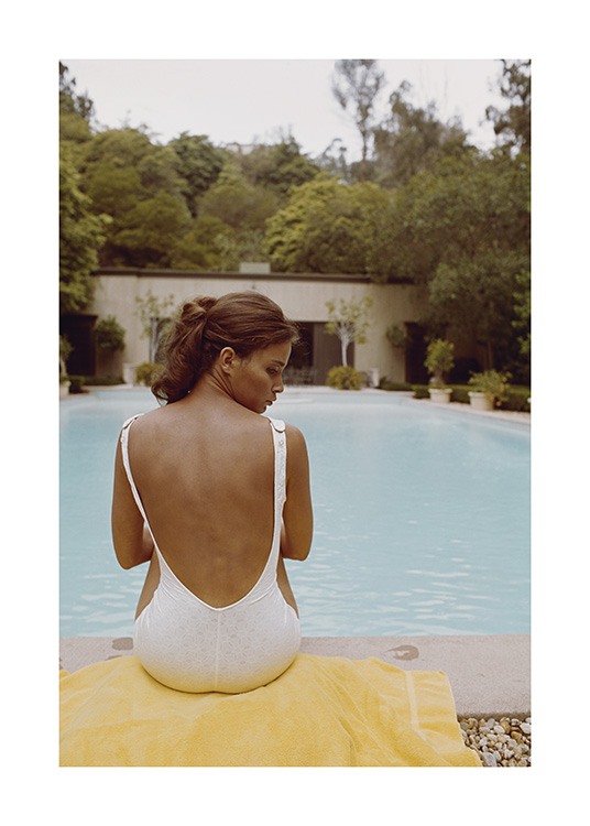  – Fotografia di una donna seduta su un asciugamano giallo davanti a una piscina in costume intero bianco