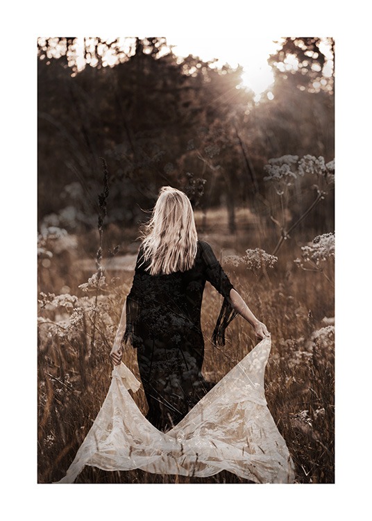  – Fotografia di una donna in abito nero che cammina in un prato tenendo un tessuto di pizzo bianco dietro di sé