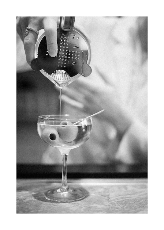  – Fotografia in bianco e nero di un martini versato da uno shaker per cocktail in un bicchiere con olive