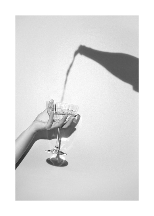  – Fotografia in grigio dell’ombra di una bottiglia di champagne e una mano che tiene un bicchiere di champagne