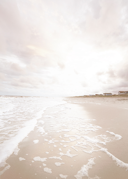  – Fotografia di una spiaggia beige con schiuma marina che la lambisce e case sullo sfondo