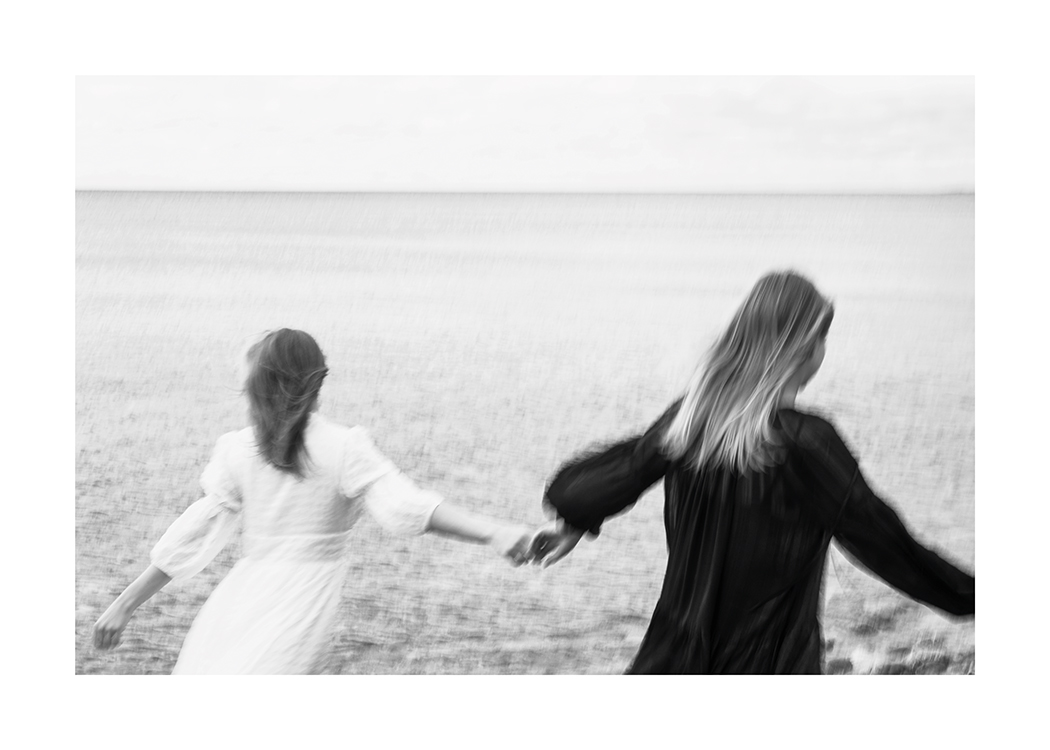  – Fotografia in bianco e nero di due donne che corrono in un prato tenendosi per mano