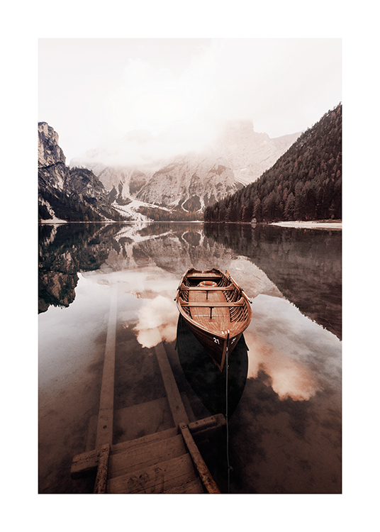  – Fotografia di un lago immobile con una piccola barca di legno e montagne innevate sullo sfondo