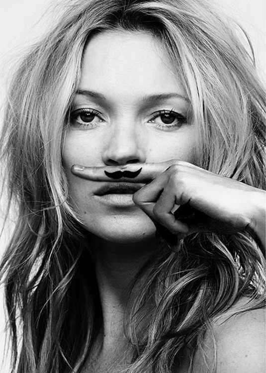  – Fotografia in bianco e nero di Kate Moss con l’indice sul labbro superiore e baffi sull’indice